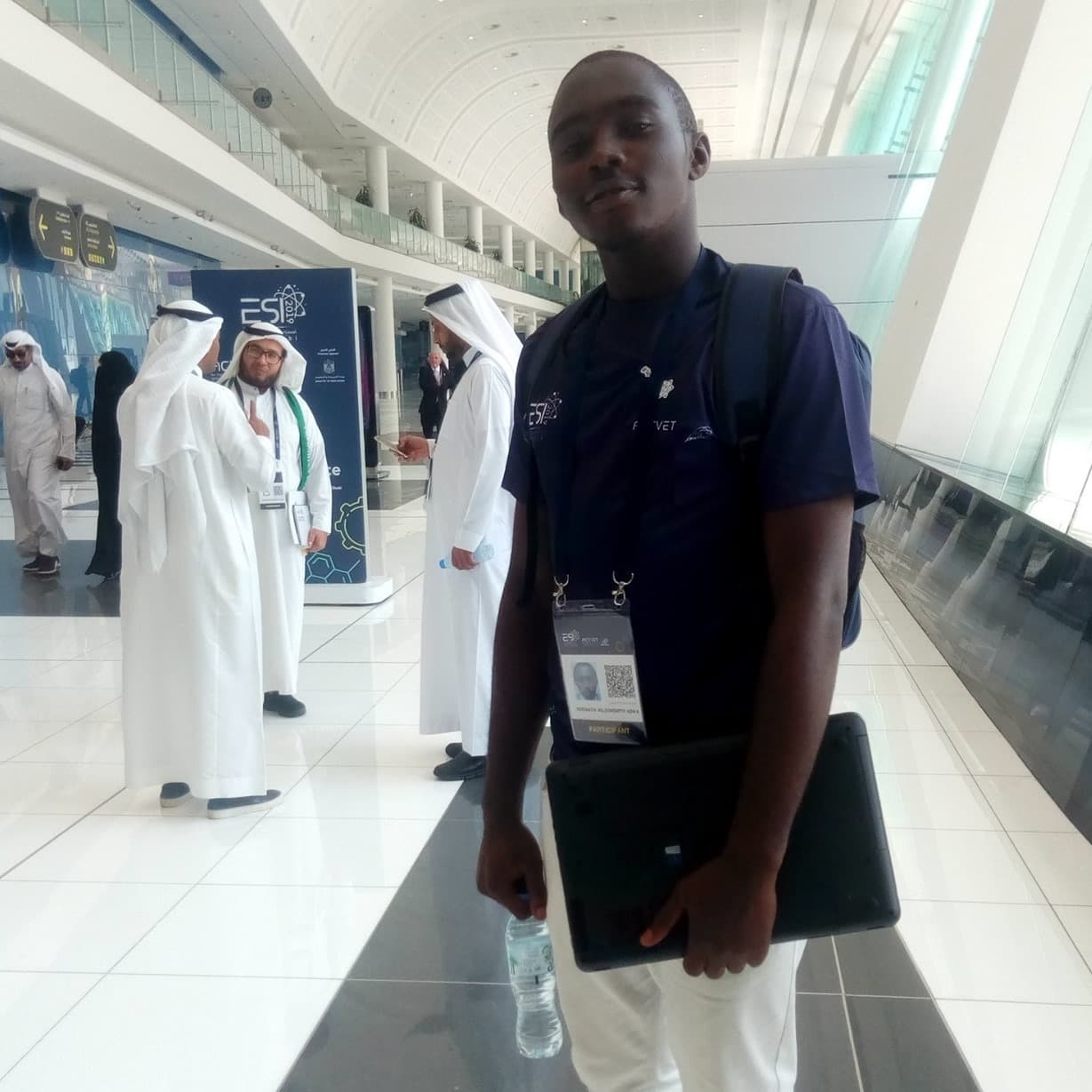 Ndemafia Wilsmith wearing an ESI 2019 participant badge and carrying a laptop in the exhibition concourse in Abu Dhabi.