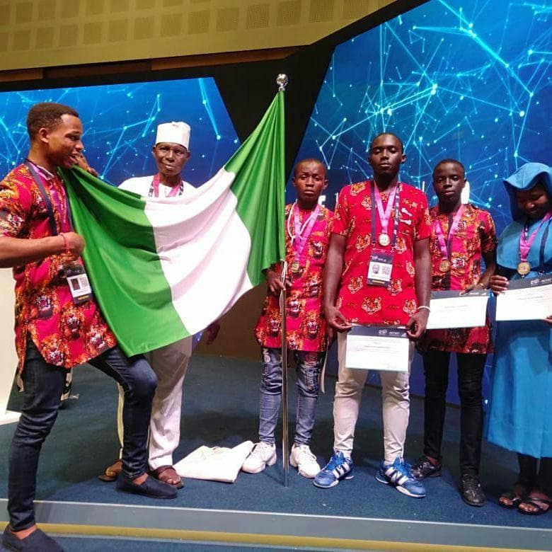 The Nigerian delegation on stage holding the national flag, wearing medals and holding certificates.
